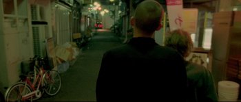 Movie still from “Enter the Void” (2009), directed by Gaspar Noé – A man with a shaved head walking down a street; Close Up shot, Over the shoulder angle