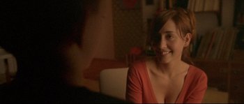 Movie still from “Enter the Void” (2009), directed by Gaspar Noé – A woman sitting on a couch smiling at the camera; Close Up shot, Over the shoulder angle