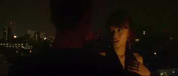 Movie still from “Enter the Void” (2009), directed by Gaspar Noé – A young woman standing next to a man in the dark; Close Up shot, Over the shoulder angle