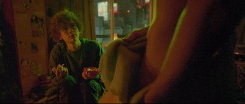 Movie still from “Enter the Void” (2009), directed by Gaspar Noé – A woman sitting in a room holding a bowl of food; Medium shot, Low angle