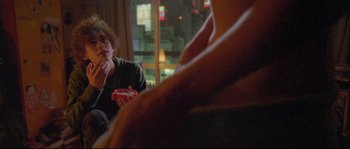 Movie still from “Enter the Void” (2009), directed by Gaspar Noé – A man sitting at a table eating a piece of pizza; Medium shot, Over the shoulder angle