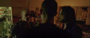 Movie still from “Enter the Void” (2009), directed by Gaspar Noé – Two people are talking in a room with a wall; Medium shot, Over the shoulder angle