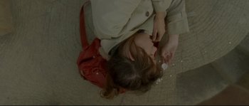 Movie still from “Enter the Void” (2009), directed by Gaspar Noé – A woman sitting on the ground with a red purse; Close Up shot, Overhead angle