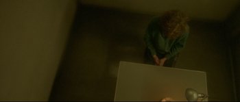 Movie still from “Enter the Void” (2009), directed by Gaspar Noé – A woman standing in a dark room next to a table; Wide shot, Overhead angle