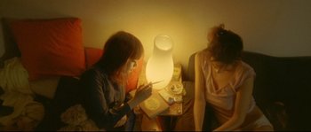 Movie still from “Enter the Void” (2009), directed by Gaspar Noé – Two women sitting at a table looking at a phone; Medium shot, High angle