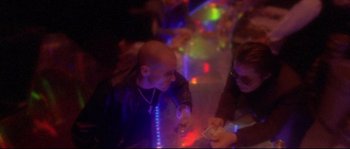 Movie still from “Enter the Void” (2009), directed by Gaspar Noé – Two people are sitting in a room with lights; Medium shot, Over the shoulder angle