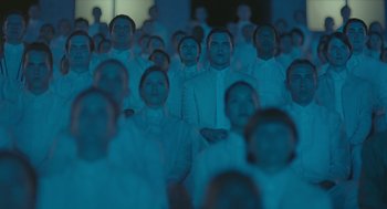 Movie still from “Equals” (2015), directed by Drake Doremus – A large group of people in a room; Wide shot, High angle