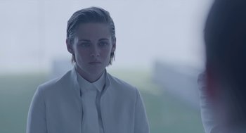 Movie still from “Equals” (2015), directed by Drake Doremus – A woman in a white jacket is standing in front of a blurry background; Close Up shot, Over the shoulder angle