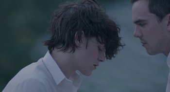 Movie still from “Equals” (2015), directed by Drake Doremus – A young man with long dark hair wearing a white dress shirt; Close Up shot, Over the shoulder angle