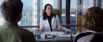 Movie still from “Game Night” (2018), directed by John Francis Daley – A woman sitting at a desk in front of papers; Medium shot, Over the shoulder angle