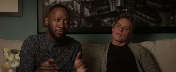 Movie still from “Game Night” (2018), directed by John Francis Daley – Two men sitting on a couch in front of a wall; Close Up shot, Over the shoulder angle