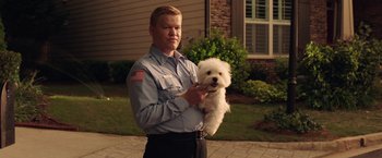 Movie still from “Game Night” (2018), directed by John Francis Daley – A man holding a small white dog in his arms; Medium shot, Over the shoulder angle