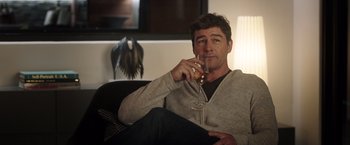 Movie still from “Game Night” (2018), directed by John Francis Daley – A man sitting on a couch holding a glass of wine; Medium shot, Over the shoulder angle