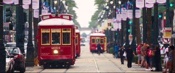 Movie still from “Girls Trip” (2017), directed by Malcolm D. Lee – Two red trolleys on a street with people on the sidewalk; Extreme Wide shot, High angle