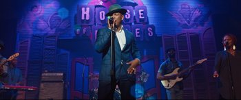 Movie still from “Girls Trip” (2017), directed by Malcolm D. Lee – A man in a green hat singing into a microphone; Wide shot, Low angle