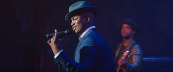 Movie still from “Girls Trip” (2017), directed by Malcolm D. Lee – A man wearing a blue suit and a blue hat singing into a microphone; Medium shot, Over the shoulder angle