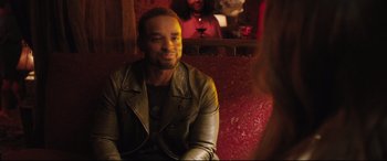 Movie still from “Girls Trip” (2017), directed by Malcolm D. Lee – A man in a leather jacket sitting on a red couch; Medium shot, Over the shoulder angle