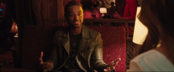Movie still from “Girls Trip” (2017), directed by Malcolm D. Lee – A man in a leather jacket sitting on a red couch; Medium shot, Over the shoulder angle