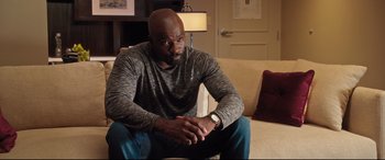 Movie still from “Girls Trip” (2017), directed by Malcolm D. Lee – A man sitting on a couch looking at his watch; Medium shot, Over the shoulder angle