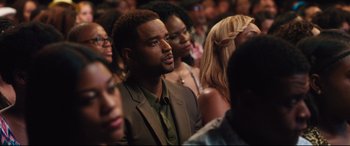 Movie still from “Girls Trip” (2017), directed by Malcolm D. Lee – A crowd of people in a room with a man in a brown suit; Close Up shot, Over the shoulder angle
