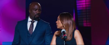 Movie still from “Girls Trip” (2017), directed by Malcolm D. Lee – A man and a woman are standing next to a microphone; Medium shot, Over the shoulder angle