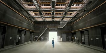 Movie still from “Evangelion: 3.0+1.01 Thrice Upon a Time” (2021), directed by Joe Fria – A man standing in a large room with a door open; Extreme Wide shot, Low angle