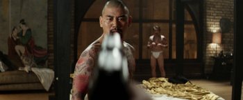 Movie still from “Everly” (2014), directed by Joe Lynch – A man with tattoos is holding a gun in front of another man; Medium shot, Over the shoulder angle