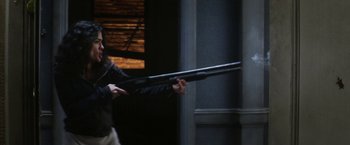 Movie still from “Everly” (2014), directed by Joe Lynch – A man holding a rifle in a dark room; Medium shot, Over the shoulder angle