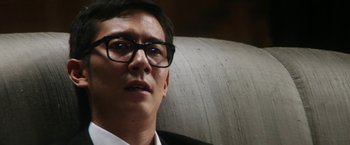 Movie still from “Everly” (2014), directed by Joe Lynch – A person wearing a suit and glasses; Close Up shot, Low angle