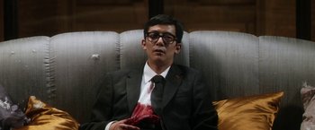 Movie still from “Everly” (2014), directed by Joe Lynch – A man in a suit and tie sitting on a couch; Medium shot, High angle
