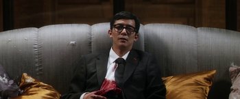 Movie still from “Everly” (2014), directed by Joe Lynch – A man in a suit and tie sitting on a couch; Medium shot, High angle
