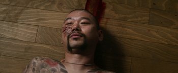 Movie still from “Everly” (2014), directed by Joe Lynch – A man with a tattoo on his face laying on the ground; Close Up shot, Overhead angle