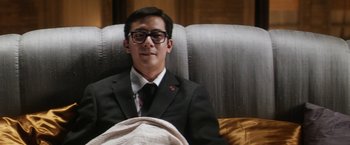 Movie still from “Everly” (2014), directed by Joe Lynch – A man in a suit and tie sitting in a chair; Medium shot, Low angle