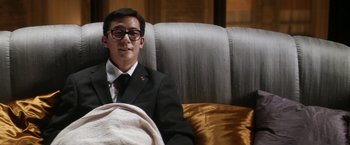 Movie still from “Everly” (2014), directed by Joe Lynch – A man sitting on a couch wearing a suit and tie; Medium shot, Low angle