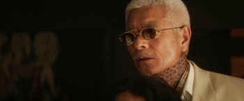 Movie still from “Everly” (2014), directed by Joe Lynch – An older man wearing glasses and a neck tattoo; Close Up shot, Low angle