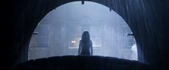 Movie still from “Everly” (2014), directed by Joe Lynch – A woman sitting on a couch under a rain covered window; Wide shot, Low angle