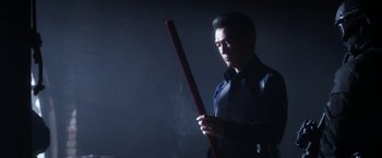 Movie still from “Everly” (2014), directed by Joe Lynch – A man holding a red stick in a dark room; Medium shot, Low angle