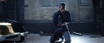 Movie still from “Everly” (2014), directed by Joe Lynch – A man kneeling on the ground looking at his cell phone; Medium shot, Low angle