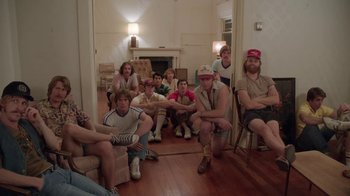 Movie still from “Everybody Wants Some!!” (2016), directed by Richard Linklater – A group of men sitting in a living room together; Wide shot, High angle