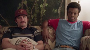 Movie still from “Everybody Wants Some!!” (2016), directed by Richard Linklater – Two men sitting on a couch in a living room; Medium shot, Over the shoulder angle