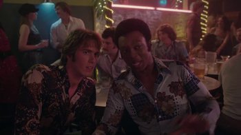 Movie still from “Everybody Wants Some!!” (2016), directed by Richard Linklater – Two men sitting at a table in front of other people; Medium shot, Over the shoulder angle