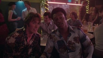 Movie still from “Everybody Wants Some!!” (2016), directed by Richard Linklater – A man and a woman sitting at a table in front of other people; Medium shot, Over the shoulder angle