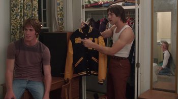 Movie still from “Everybody Wants Some!!” (2016), directed by Richard Linklater – A man holding a jacket in a room with other people; Medium shot, Over the shoulder angle
