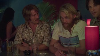 Movie still from “Everybody Wants Some!!” (2016), directed by Richard Linklater – A couple of men sitting at a table with drinks; Medium shot, Over the shoulder angle