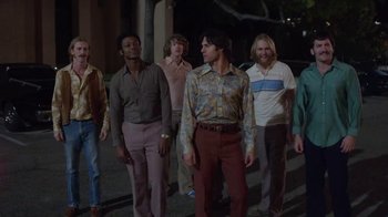 Movie still from “Everybody Wants Some!!” (2016), directed by Richard Linklater – A group of men standing next to each other on a sidewalk; Wide shot, Low angle
