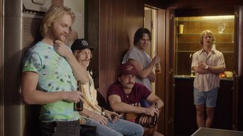 Movie still from “Everybody Wants Some!!” (2016), directed by Richard Linklater – A group of men sitting next to each other holding beers; Medium shot, Low angle