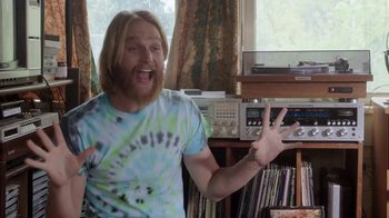 Movie still from “Everybody Wants Some!!” (2016), directed by Richard Linklater – A man in a tie dye t - shirt standing in front of a record player; Medium shot, Over the shoulder angle