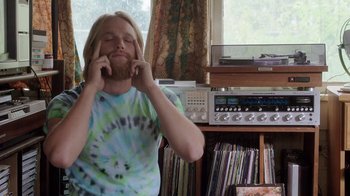 Movie still from “Everybody Wants Some!!” (2016), directed by Richard Linklater – A man with long blonde hair is sitting in front of a record player; Medium shot, High angle