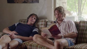 Movie still from “Everybody Wants Some!!” (2016), directed by Richard Linklater – Two men sitting on a couch reading a book; Medium shot, Low angle