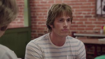Movie still from “Everybody Wants Some!!” (2016), directed by Richard Linklater – A man with long brown hair sitting in front of a brick wall; Close Up shot, Over the shoulder angle